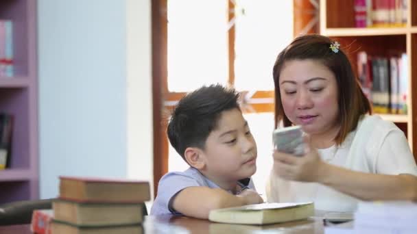 Happy asian boy and mother are take a photo by cell phone in library - Footage, Video