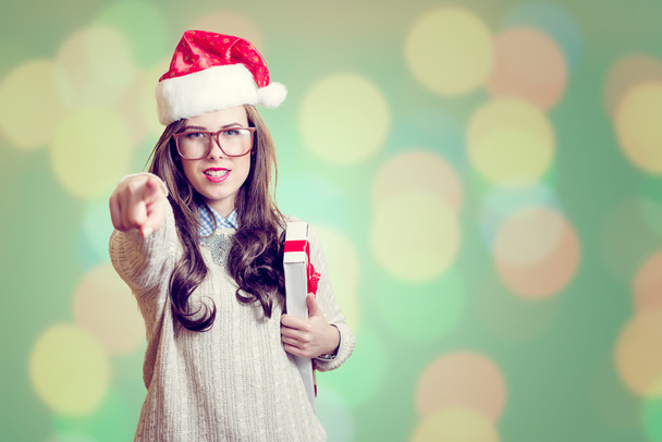 Picture of pointing finger and holding present box beautiful young lady in Santa Claus hat on abstract festive background design - Zdjęcie, obraz