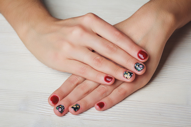 Red nail art with printed flowers on wooden background - 写真・画像