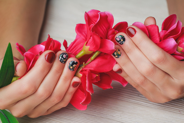 Red nail art with printed flowers on wooden background - 写真・画像