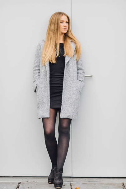 Blonde young woman standing behind the wall and posing ti camera - Fotó, kép