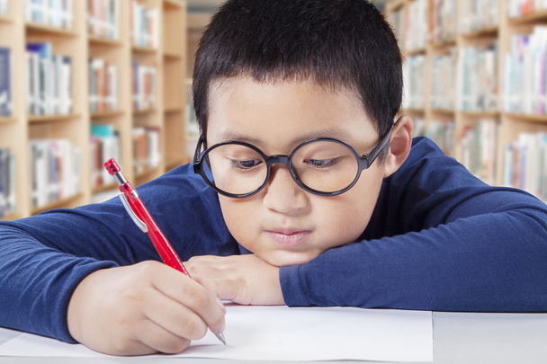 Menino usando uma caneta para escrever no papel na biblioteca
 - Foto, Imagem