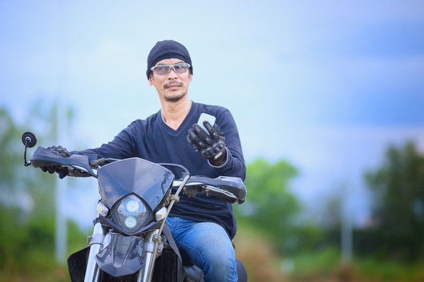 Aasia komea mies moottoripyöräilijä soittaa puhelimeen moottoripyörällä
  - Valokuva, kuva