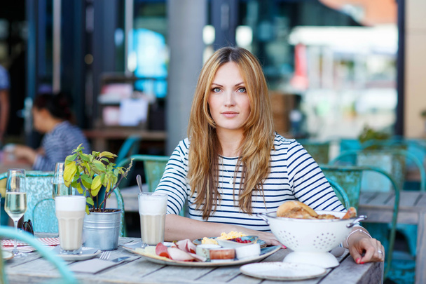 Молодая женщина, завтракающая в кафе на открытом воздухе
 - Фото, изображение