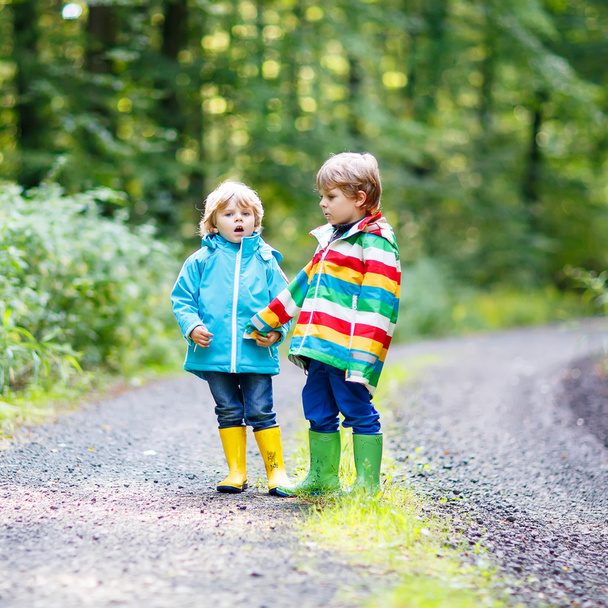 zwei kleine Geschwister in bunten Regenmänteln und Stiefeln gehen - Foto, Bild
