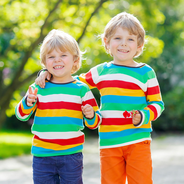 Two little kid boys in colorful clothing walking hand in hand - Фото, изображение