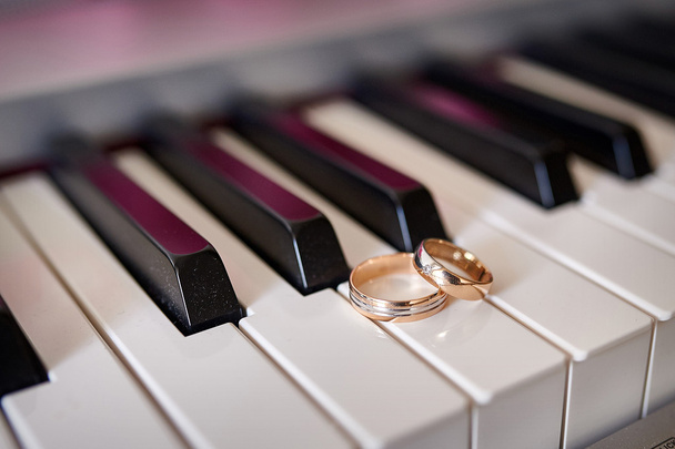 Золотые обручальные кольца лежат на клавишах пианино
 - Фото, изображение