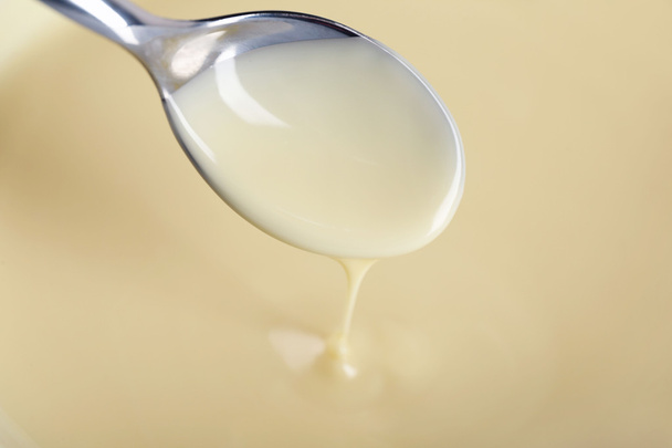 Background of condensed milk and a spoon in a bowl, close-up - Fotoğraf, Görsel