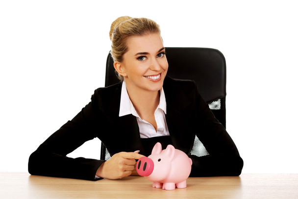 Businesswoman with a piggybank behind the desk - Foto, afbeelding