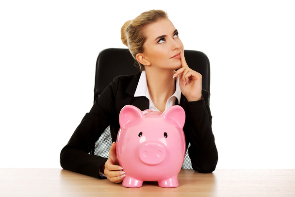 Businesswoman with a piggybank behind the desk - Zdjęcie, obraz