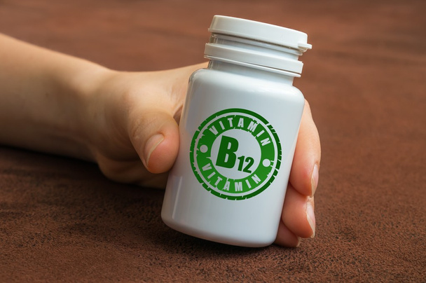 Mano humana sosteniendo un frasco de pastillas con vitamina B12
 - Foto, Imagen