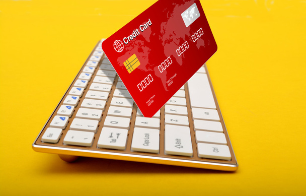 Keyboard key holding a credit card on yellow background - Photo, Image