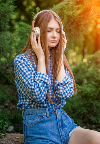 Young woman cute brunette girl sitting on stone headphones - Foto, afbeelding