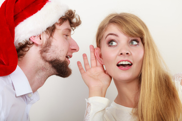 Man in santa hat whispering to woman ear. - Foto, imagen