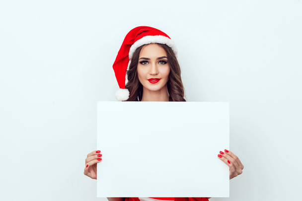 Beautiful girl in the hat of Santa Claus. Hold a sheet of paper. Red manicure. Red lips. - Foto, Bild