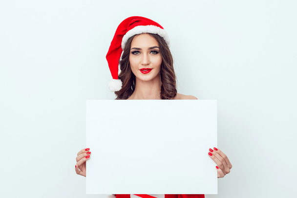 Beautiful girl in the hat of Santa Claus. Hold a sheet of paper. Red manicure. Red lips. - Φωτογραφία, εικόνα