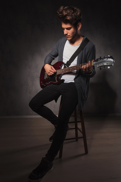 artista indie che suona la chitarra seduto su una sedia in studio
 - Foto, immagini