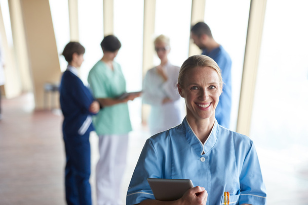 naislääkäri, jolla on tabletin tietokone, seisoo taustalla olevan tiimin edessä, sairaalan hoitohenkilökunta
 - Valokuva, kuva