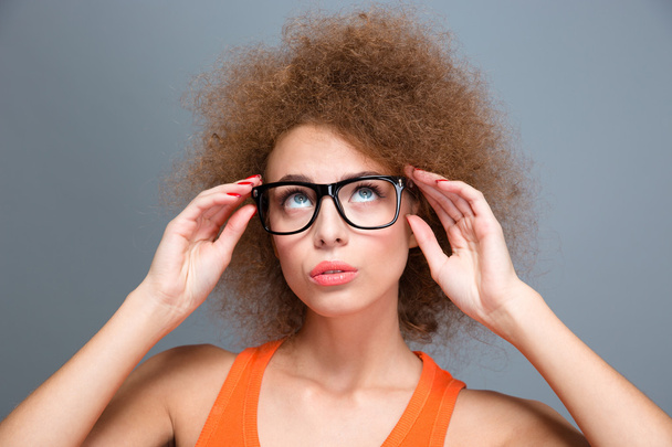 Mujer rizada joven concentrada en gafas negras mirando hacia arriba
 - Foto, Imagen