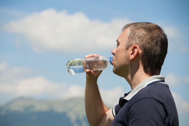 Ένας άνθρωπος πίνει νερό από ένα μπουκάλι στα βουνά - Φωτογραφία, εικόνα
