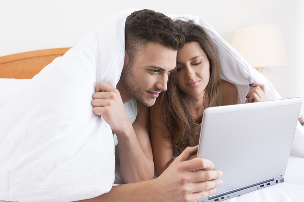 Young couple snuggled under the cover with laptop - Foto, afbeelding