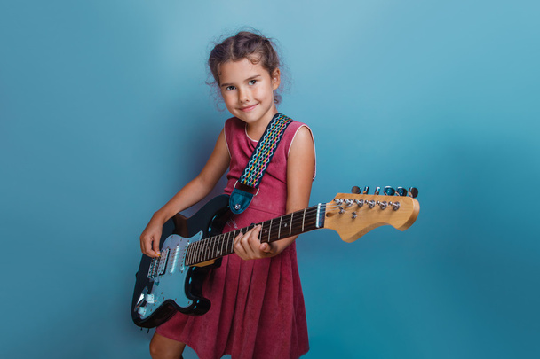 Menina aparência europeia dez anos tocando guitarra em um bac azul
 - Foto, Imagem