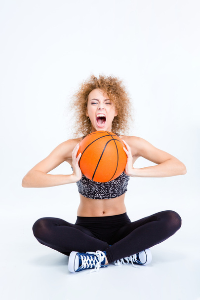 Woman sitting on the floor with basketball ball and screaming - 写真・画像