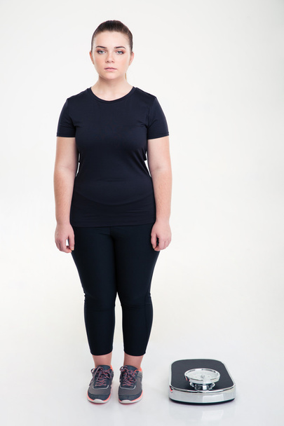 Serious fat woman standing near weighing machine - Foto, imagen