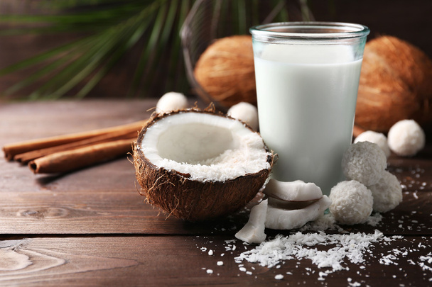 Candies in coconut flakes, glass of milk and fresh coconut on dark wooden background - Foto, Imagen