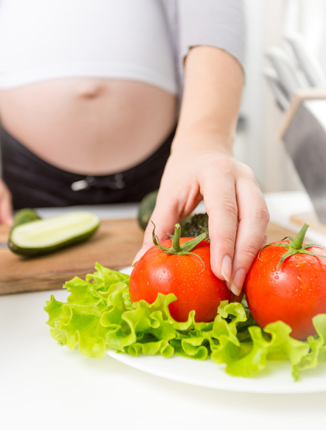 Gros plan de la femme enceinte prenant tomate fraîche de l'assiette
 - Photo, image