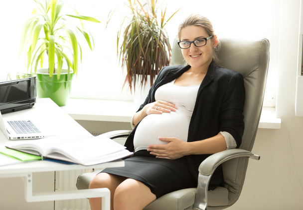 Felice donna d'affari incinta in posa sulla sedia in ufficio
 - Foto, immagini