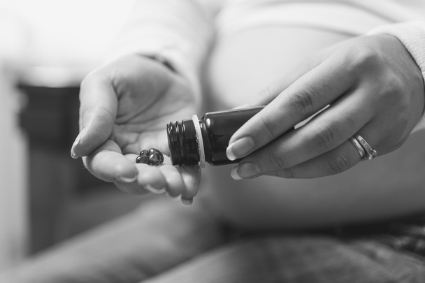 Black and white photo of pregnant woman holding pills on hand - Photo, Image