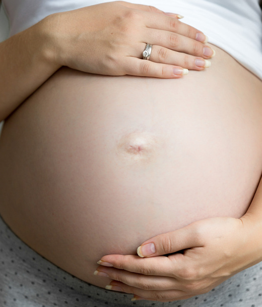 Nahaufnahme einer schwangeren Frau, die Hände auf dickem Bauch hält - Foto, Bild