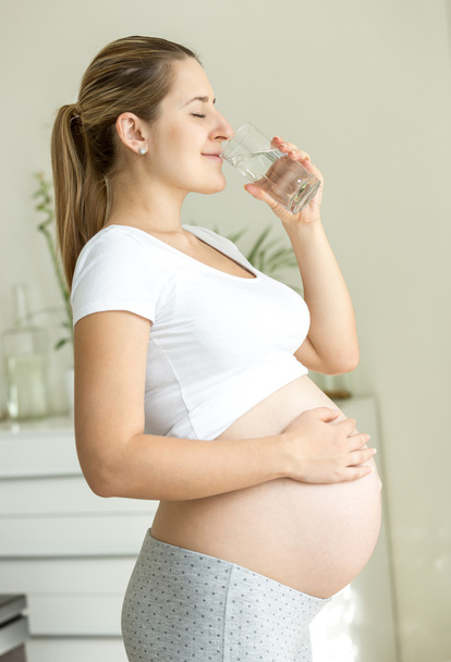 beautiful pregnant woman drinking water at living room - Zdjęcie, obraz