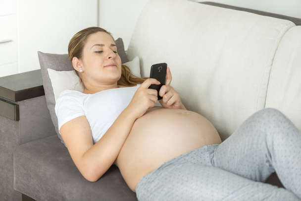 вагітна жінка лежить на дивані і використовує смартфон
 - Фото, зображення