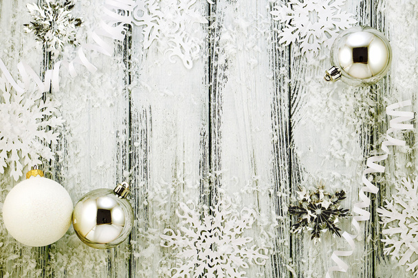 Новогодняя тема: елочные украшения белого и серебристого цвета, шары, снег, снежинки, серпантин на белом ретро-стилизованном деревянном фоне с желтой подсветкой
 - Фото, изображение