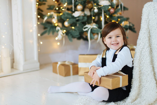 Mała dziewczynka uśmiechający się w pobliżu choinki i prezenty. - Zdjęcie, obraz