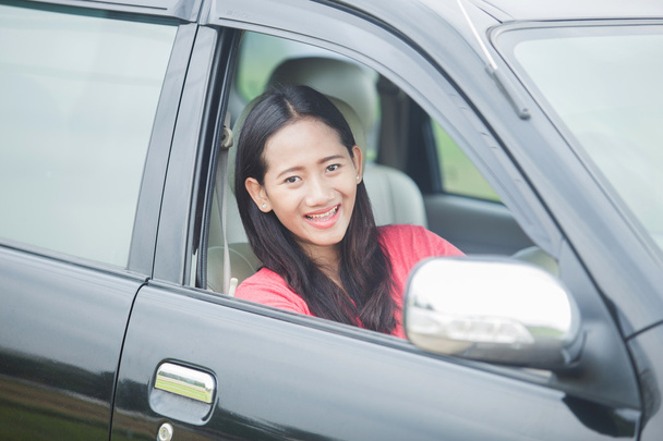 Young Asian woman driving a car, smiling to the camera - Фото, изображение