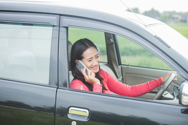 Young Asian woman talking on the phone while driving a car - Фото, зображення