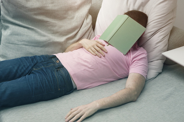man sleeping on couch with book on his head - 写真・画像