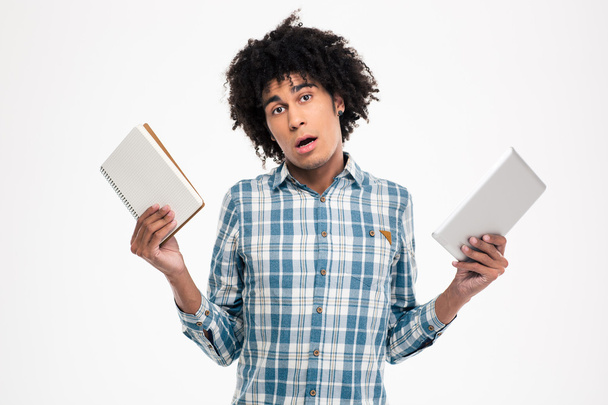 Afro american man choosing between paper book or tablet computer - 写真・画像