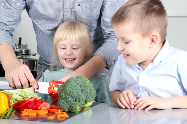 Smiling cute daughter and son  cooking  a  dinner. Little children  chopping  a  colorful pepper with father. - Foto, Bild