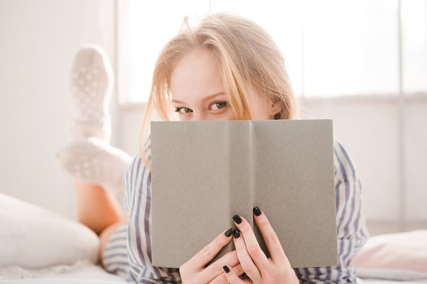 Flirty shy young woman covered her face by the book - Foto, Bild