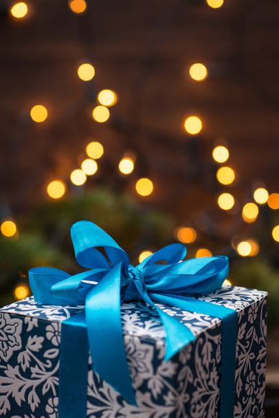 Χριστουγεννιάτικο δώρο κουτί με μπλε τόξο και φώτα σε ξύλινη επιφάνεια - Φωτογραφία, εικόνα