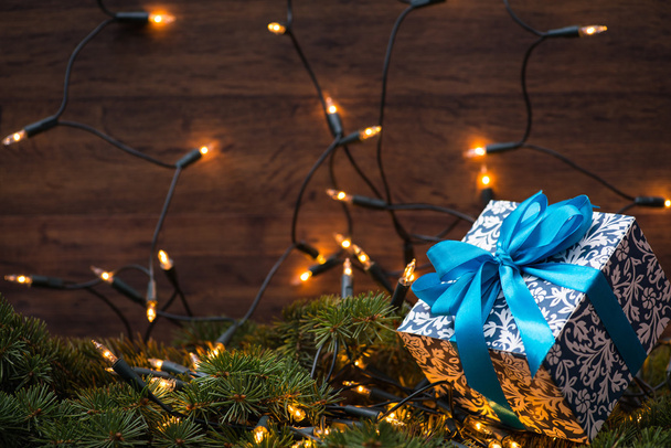 Χριστούγεννα δώρο κουτί με μπλε τόξο και φώτα σε ένα κλαδί έλατου - Φωτογραφία, εικόνα