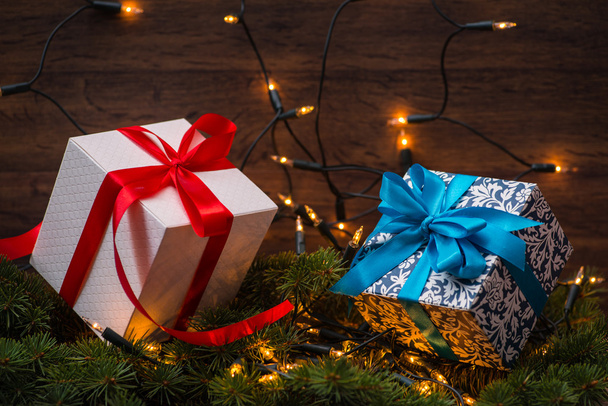 Weihnachtsgeschenkboxen mit roten und blauen Schleifen und Lichtern auf Holzoberfläche - Foto, Bild