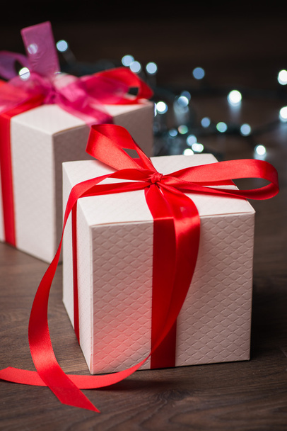 Kerstmis geschenkdozen met rode boog en lichten op houten oppervlak - Foto, afbeelding