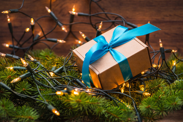 Рождественская подарочная коробка с голубым луком и огнями на елке
 - Фото, изображение
