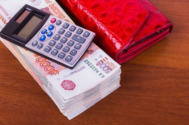 A bundle of money, red leather wallet and calculator are on the table - Photo, image
