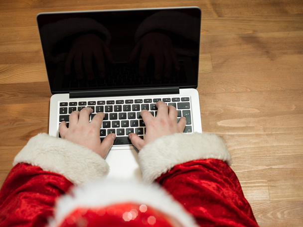 Santa working at desk and typing on a laptop, Christmas gifts and letters, hands top view - Фото, изображение